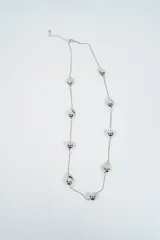Collar largo de cadena fina plateada con dijes esféricos y orgánicos distribuidos a lo largo de la pieza.