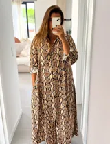 Vestido camisero midi con estampado de piel de serpiente, corte holgado, cierre frontal con botones y mangas largas con puños vueltos.