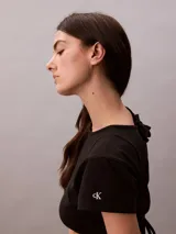 Remera cropped de algodón con corte boxy, cuello redondo y mangas cortas. Presenta un bajo redondeado en la parte delantera y un diseño con espalda abierta y lazo decorativo.