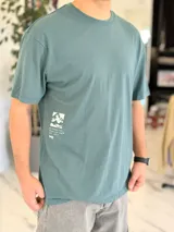 Remera oversize verde con estampado gráfico en la espalda con diseño de paisaje oriental y texto.