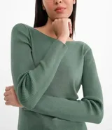 Suéter de punto color rosado, con cuello barco, mangas largas y puños con botones decorativos. El dobladillo también es acanalado.