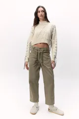 Sweater de lana merino tejido en punto grueso, color gris oscuro, con cuello alto. Presenta un diseño calado con tientos de cuero marrón insertados a lo largo de la prenda, simulando un lazo o detalle orgánico.