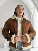 Chaqueta marrón con cuello de piel sintética color crema, cierre frontal con cremallera y hebilla en el cuello, bolsillos laterales con ribete de cuero marrón y puños con ribete de piel sintética.