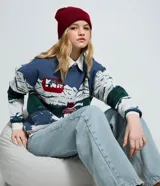 Suéter de punto jacquard de manga larga y cuello redondo con diseño invernal que incluye montañas, un teleférico rojo y un oso esquiando, con terminaciones caneladas en puños y ruedo.