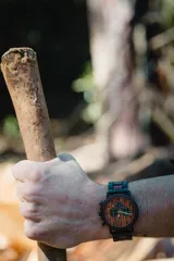 Reloj multifuncional para hombre, con caja de madera de sándalo rojo y acero inoxidable negro. La esfera es de madera de sándalo rojo con subdiales negros funcionales que ofrecen cronógrafo, indicador de 24 horas y fechador. La malla es de acero inoxidable negro con incrustaciones de madera de sándalo rojo.
