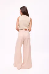 Pantalón de tiro alto, pierna ancha y largo, color beige claro con finas rayas verticales en tono oscuro. Presenta un diseño de cinco bolsillos estilo jean.