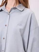 Camisa de manga larga con efecto lavado, corte oversize y cierre frontal con botones. Presenta cuello clásico y logo bordado en el pecho.