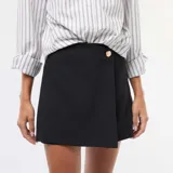 Falda pantalón de color negro con diseño asimétrico y cierre frontal con botón dorado decorativo.