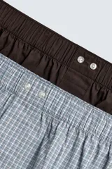 Pack de dos calzoncillos tipo bóxer de popelina de algodón, con cintura elástica y bragueta con botones. Incluye un bóxer liso en color marrón oscuro y un bóxer con estampado a cuadros en tonos celestes y blancos.