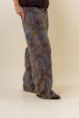 Jean de corte wide leg con estampado floral en tonos tierra sobre base de denim gris oscuro. Presenta tiro medio-alto, bolsillos traseros funcionales y costuras reforzadas.