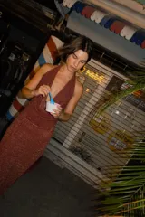 Falda larga tejida color marrón con brillo metálico, corte al cuerpo, abertura alta en la pierna y recortes laterales con cordones ajustables.