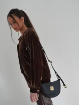 Bandolera de cuero color beige con correa ajustable y logo metálico dorado en el frente.