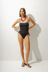 Malla enteriza negra con breteles finos, escote recto y laterales fruncidos con cordones ajustables.