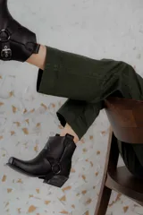 Botinetas de cuero negro con diseño estilo western, punta cuadrada y taco bajo con acabado desgastado. Presentan una tira decorativa con estribo metálico desmontable alrededor del tobillo.