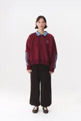 Buzo estilo rugby de corte oversized, color verde oscuro, con cuello tipo camisa en denim azul claro y cierre frontal parcial. Presenta un recorte horizontal en el pecho, logo bordado y tiras laterales en las mangas en contraste.