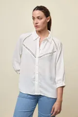 Camisa blanca de calce relajado, con mangas 3/4, cuello clásico y cierre frontal de botones. Presenta detalles calados en forma de V en la parte superior delantera.