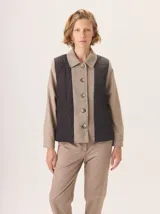 Campera de diseño híbrido que combina paneles laterales acolchados en color negro con una franja central y mangas en tejido de lana con patrón de espiga en tono beige. Presenta cuello camisero, cierre frontal con botones y forro interior de lana.