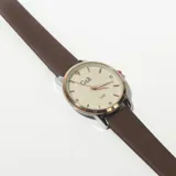 Reloj de pulsera con correa de cuero marrón y esfera redonda color crema con números arábigos y agujas doradas.