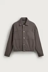 Cazadora de corte cropped fit confeccionada en tejido de algodón de color gris oscuro, con cuello solapa, manga larga con puño abotonado, bolsillos de plastrón en el pecho y cierre frontal con botonadura metálica.
