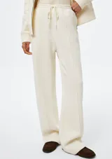 Pantalón de corte recto y holgado, color blanco, con cintura elástica y cordón ajustable. Presenta costuras verticales frontales que estilizan la silueta.