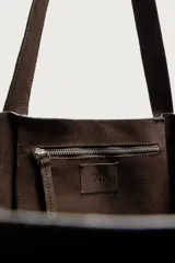 Bolso tipo shopper de gran tamaño confeccionado en piel con acabado de serraje. Presenta un diseño minimalista con costuras visibles, compartimento principal amplio y dos asas de hombro integradas.