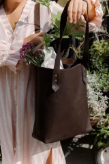 Cartera tipo tote bag de cuero marrón, con diseño minimalista, asas largas y detalles de remaches metálicos en la unión de las asas.