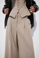 Pantalón sastrero de corte cropped y tiro alto, con piernas amplias y pliegues frontales. Presenta cierre con botón y trabillas en la cintura, en un tono beige con estampado de microcuadros.