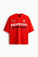 Remera de malla color rojo, con cuello en V, mangas cortas y corte oversized. Cuenta con diseño estampado frontal de Honda con banderas a cuadros y el logo de la marca.