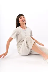 Conjunto de pijama de algodón color champagne, compuesto por una remera de manga corta con cuello henley y bolsillo en el pecho, y un pantalón capri a rayas horizontales celestes y blancas.