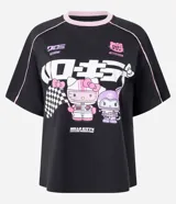 Remera de algodón negra con cuello redondo en color rosa, manga corta y diseño estilo racing. Presenta estampado frontal con personajes de Hello Kitty y Kuromi, junto con tipografía japonesa y detalles gráficos.