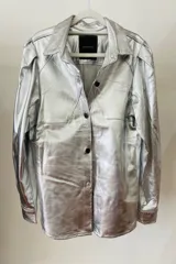 Camisa plateada de cuero sintético, de corte recto con mangas abullonadas y cierre frontal con botones negros.