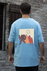 Remera celeste de algodón con estampa en la espalda de una figura humana marrón frente a montañas y un sol amarillo.