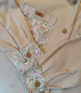 Sobre camisa beige con detalles estampados floreados en el interior de los bolsillos y en los puños, botones marrones y etiqueta de cuero con la marca Pacampa.