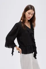 Blusa de poliéster color negro, con diseño holgado, escote en V con solapa y volados que descienden en cascada por el frente. Cuenta con mangas 3/4 con detalles de volados en los puños y en el ruedo.