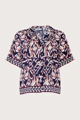 Camisa azul marino de manga corta, con cuello solapa, cierre frontal de botones y diseño estampado de estilo ikat en tonos blancos, rojos y azul marino.