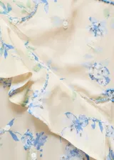 Vestido corto color crema con estampado floral en tonos azules y verdes, con escote en V, breteles finos y volados en el escote y ruedo. Presenta lentejuelas bordadas y cierre lateral invisible.