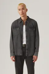 Camisa de jean estilo western en color gris lavado, con cuello clásico, cierre frontal con botones y dos bolsillos delanteros con solapa y botón. Presenta etiqueta roja distintiva en el bolsillo izquierdo.