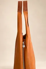 Bolso tipo tote de gamuza azul marino, de gran capacidad y diseño flexible, con asas largas de cuero marrón oscuro y placa metálica con la marca grabada en la parte frontal.