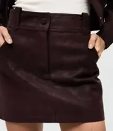 Short pollera de gamuza sintética color marrón, con cintura estructurada, botón forrado y bolsillos delanteros funcionales.