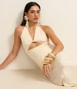 Vestido largo color crema, de tejido jersey, con escote halter y detalle de nudo/torcido en el busto que genera un recorte cutout central. El vestido es ajustado al cuerpo.
