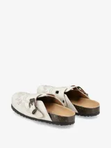 Mules color crema con diseño vaquero bordado en hilo negro. Tiene hebilla lateral para ajuste y suela de corcho.