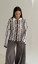 Camisa blanca de manga larga con delicados bordados florales verticales y detalles de encaje. Presenta cuello clásico, cierre frontal con botones y terminaciones festoneadas en los puños y el ruedo.