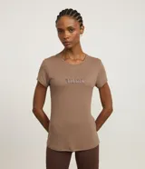 Remera deportiva femenina de manga corta y cuello redondo, color marrón topo, confeccionada en poliamida con tecnología Dry. Presenta la palabra "Balance" en relieve en el pecho.