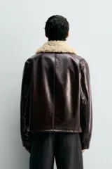 Cazadora de corte regular fit confeccionada en tejido efecto piel con acabado vinilo brillante en color marrón oscuro. Presenta cuello de solapa con tejido de borreguillo a contraste, cierre frontal de cremallera y bolsillos laterales de vivo.
