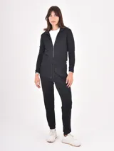 Monoprenda de estilo deportivo color negro, con cierre frontal parcial, mangas largas y cintura elástica con cordón ajustable. Presenta un diseño de pantalón tipo jogger con puños en los tobillos.