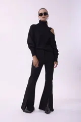 Sweater de punto negro con cuello alto y diseño asimétrico con abertura en un hombro. Presenta mangas largas con puños ajustados y corte holgado.