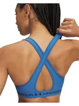 Top deportivo Under Armour Crossback Mid color azul, con diseño de tirantes cruzados en la espalda y banda elástica inferior con el nombre y logo de la marca.