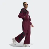 Pantalón deportivo Adidas Originals holgado de color bordó, con cintura elástica, tiro medio y detalles de tres tiras grandes negras en los laterales de las pantorrillas.
