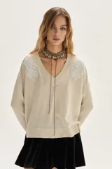 Sweater de tejido de punto con acabado brillante de lurex, escote en V y mangas largas. Presenta detalles de bordados florales en los hombros y un diseño con tajos laterales en el ruedo.