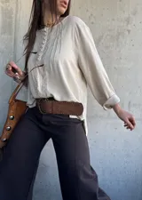 Blusa beige de corte oversize, con mangas largas, botones forrados en el frente y detalles de puntillas y alforzas verticales.